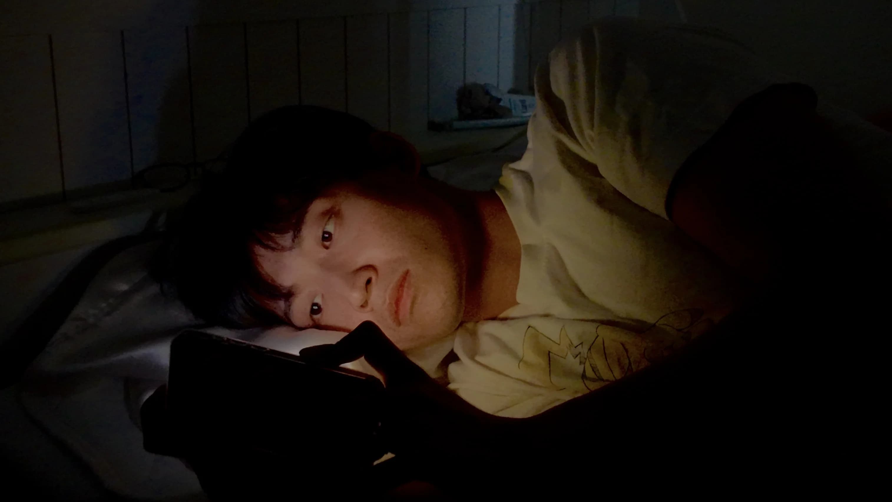 夜、暗い部屋でスマホの画面を見つめる人